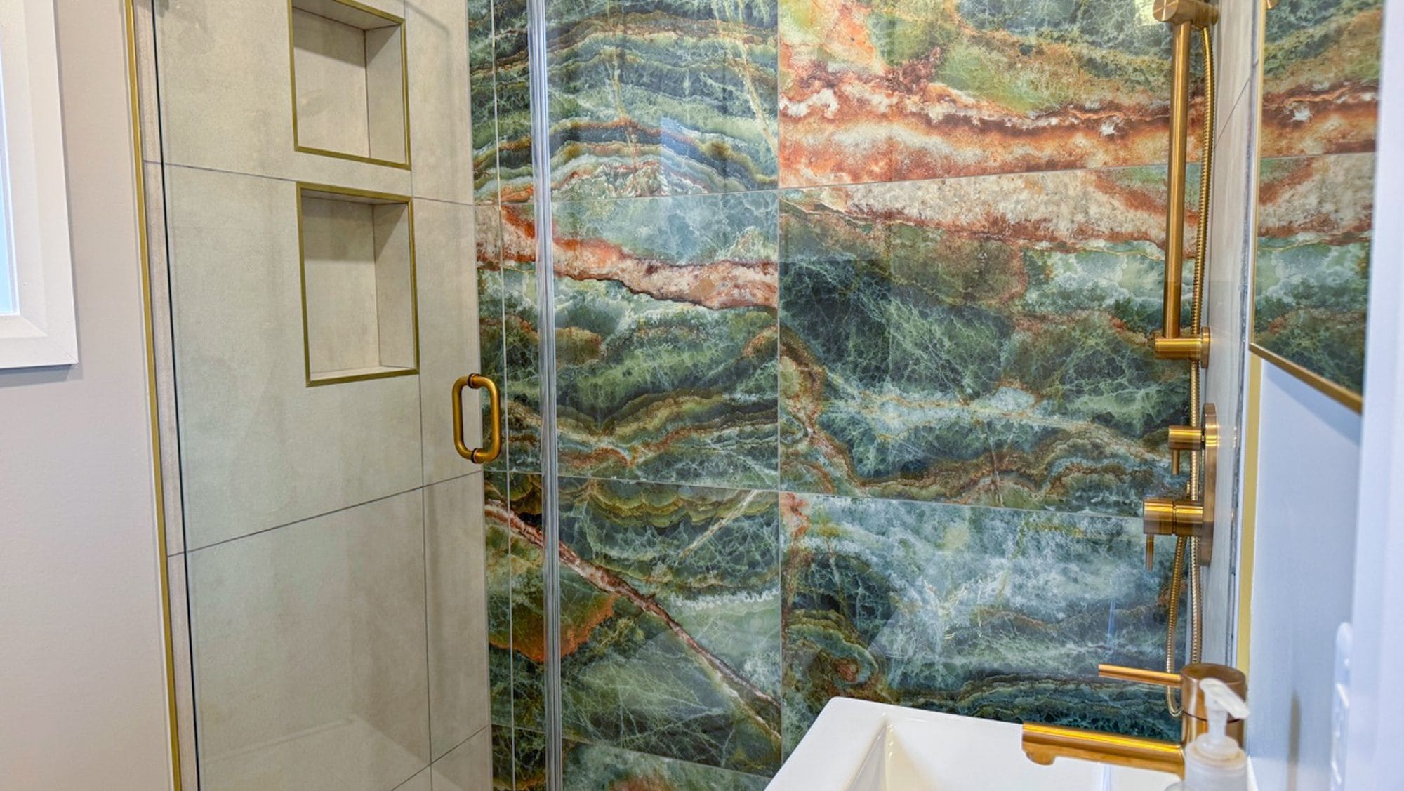 Glass shower with gold-coloured hardware, recessed shelves and a patterned tile feature wall.