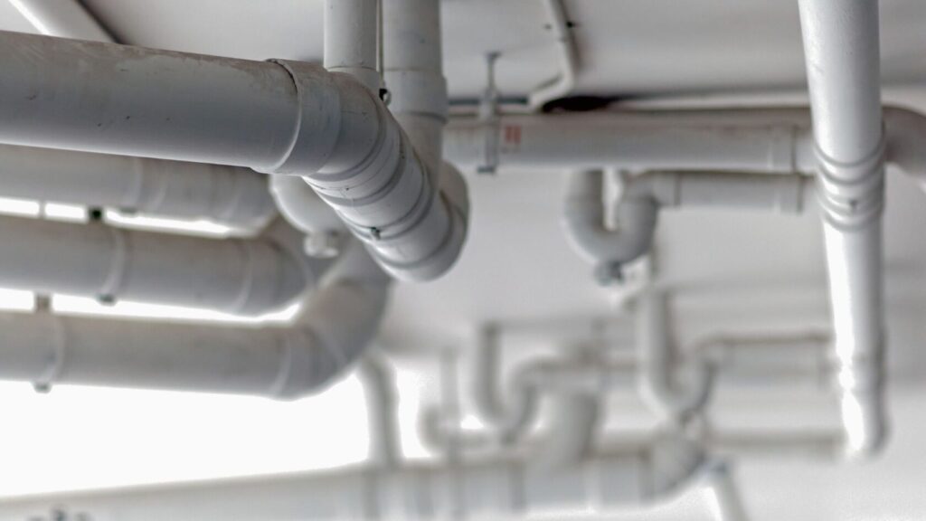 A bathroom with white walls filled with various pipes arranged in a complex network. 